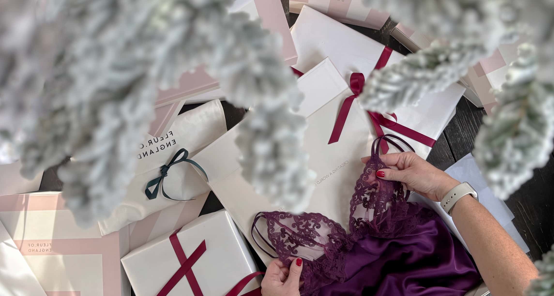 Person holding a purple lace garment with gift boxes and decorative elements in the background