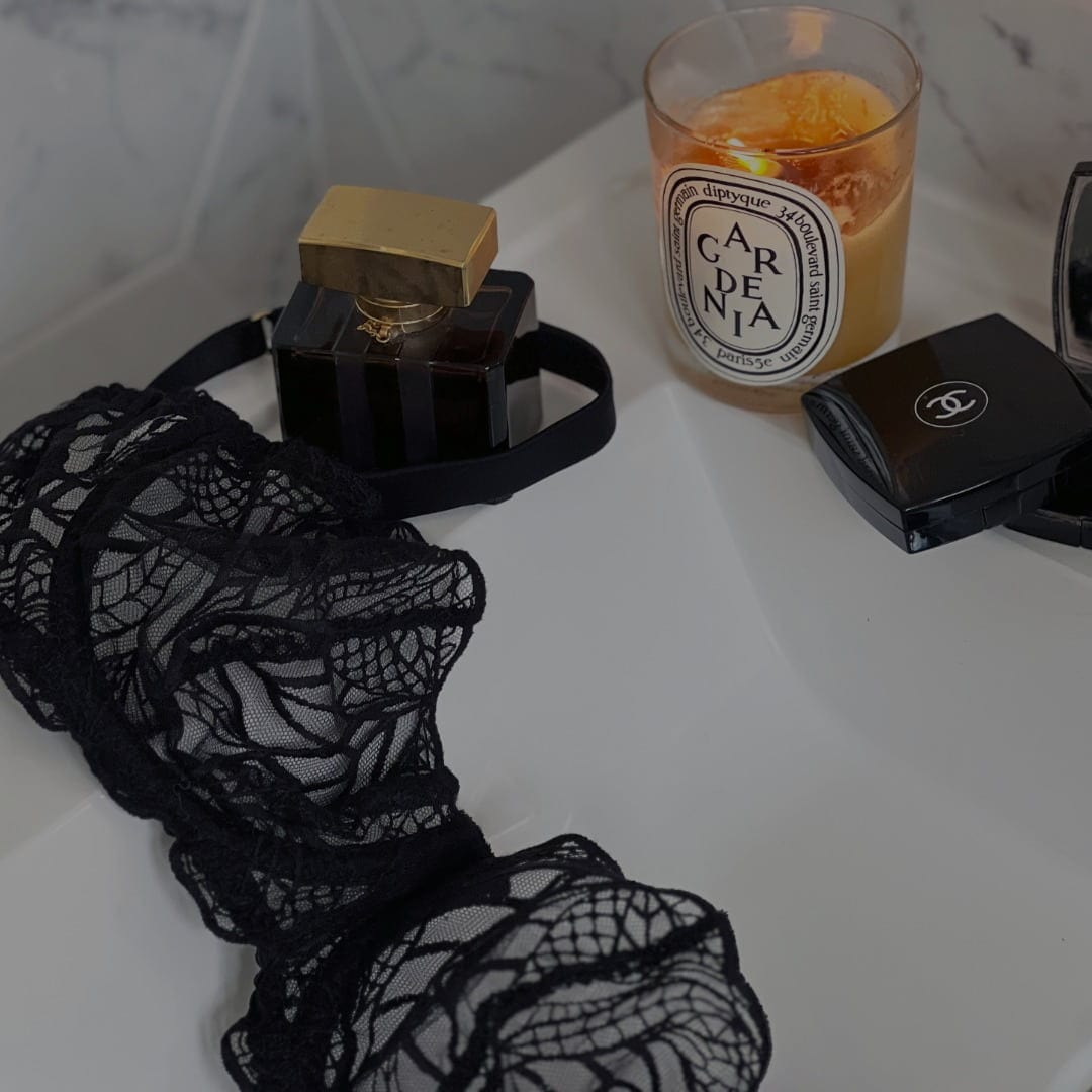 Luxury black lace bra on the sink with diptyque candle, chanel press powder and perfume bottle