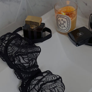 Luxury black lace bra on the sink with diptyque candle, chanel press powder and perfume bottle