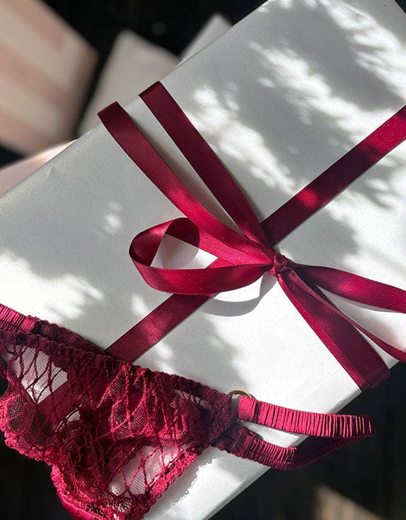 White gift box with a red ribbon and red lace lingerie on a blurred background